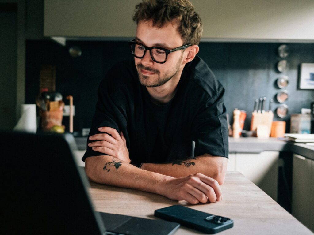 Man smiling while working on a laptop at a kitchen table
